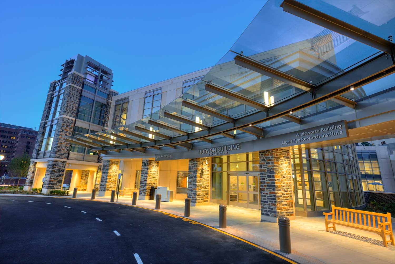 The Hudson Building at Duke Eye Center at dusk, its glass canopy and stone columns lit from within
